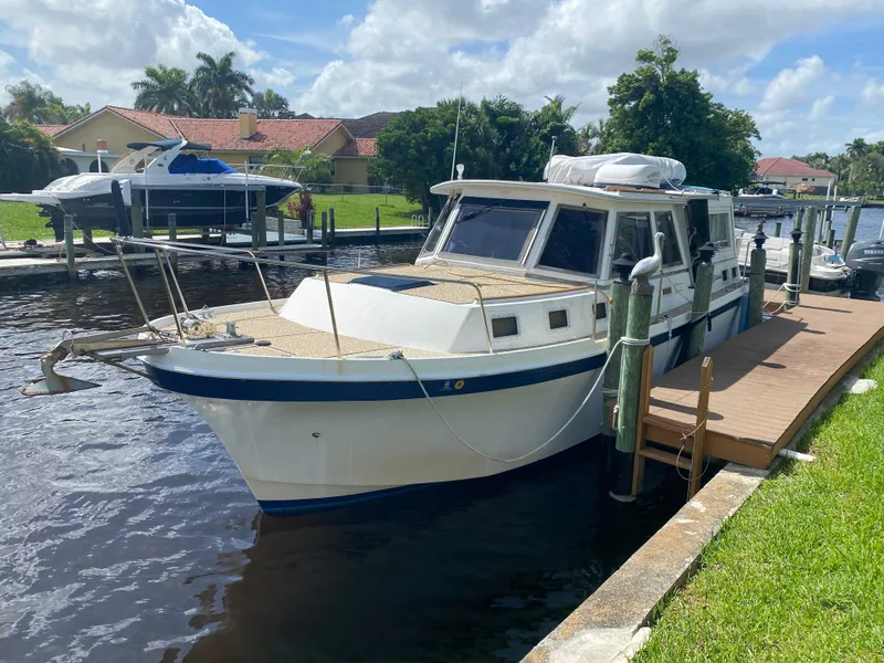 The Image of 1986 Albin 34 Family Cruiser docked by a waterfront home under a partly cloudy sky. - 0