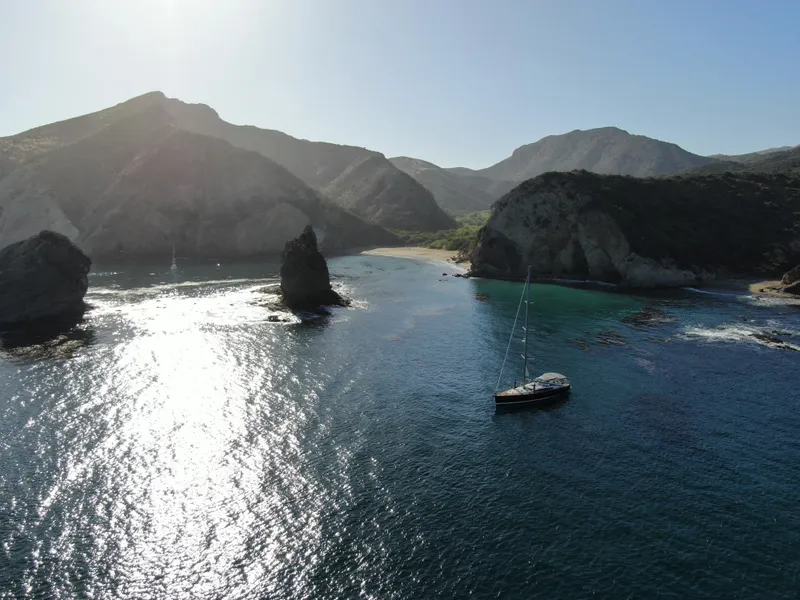 Slide: The Image of Sailboat Jeanneau 57 (2013) anchored in a scenic coastal bay with rocky cliffs. - 5
