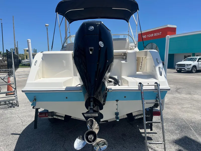 Slide: The Image of 2022 Cobia 220 Dual Console boat with outboard motor and ladder, parked outdoors. - 5