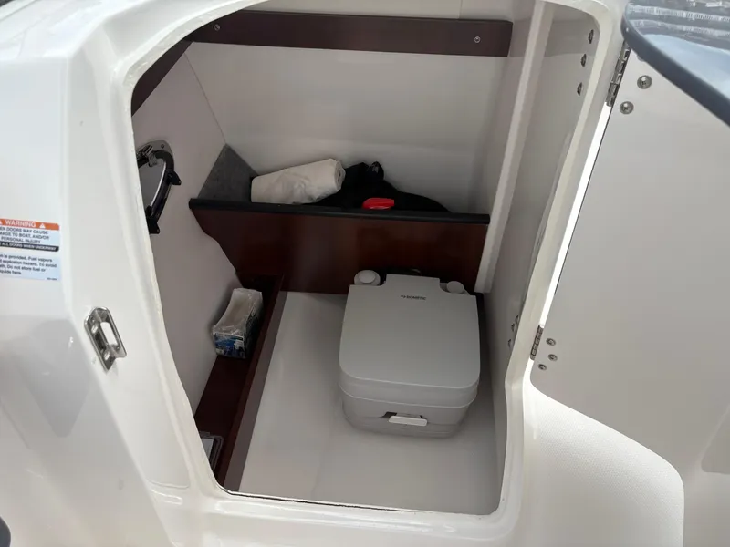 Slide: The Image of 2020 Chaparral 250 Suncoast boat interior with compact portable toilet and storage space. - 20
