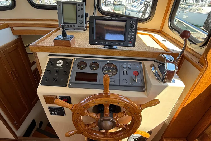 Slide: The Image of 1997 Nordic Tug 26 helm with wooden wheel, navigation instruments, and control panel. - 12