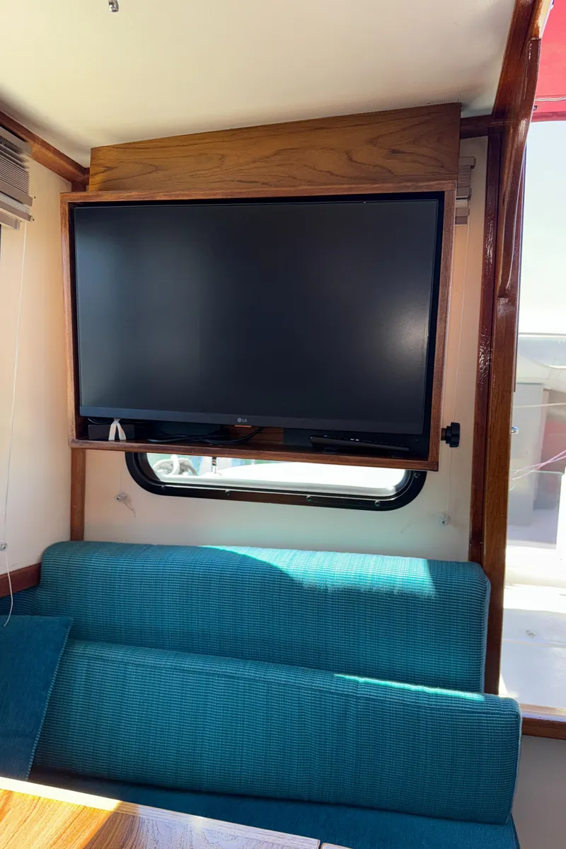 Slide: The Image of Interior of a 1997 Nordic Tug 26 with a mounted TV above a teal sofa. - 17