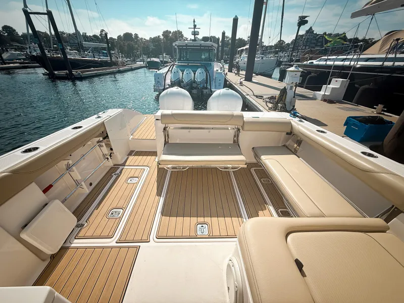 Slide: The Image of 2018 Pursuit DC 325 Dual Console boat interior at marina, featuring spacious seating and teak flooring. - 11