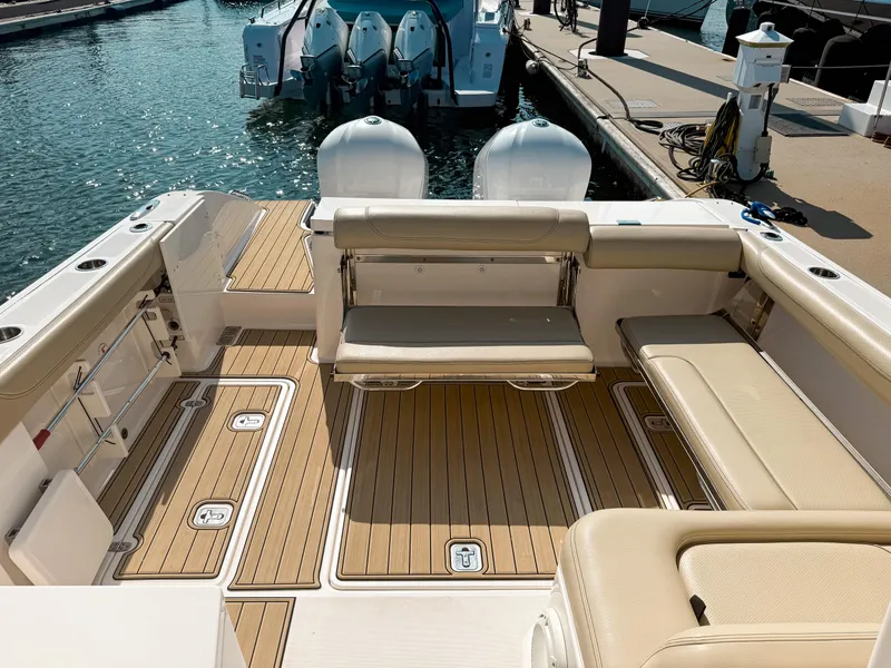 Slide: The Image of 2018 Pursuit DC 325 Dual Console boat interior with teak flooring and seating at marina. - 12