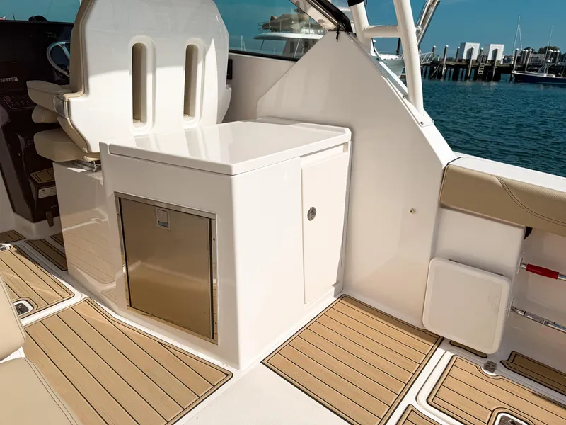 Slide: The Image of 2018 Pursuit DC 325 Dual Console interior with seating and storage, docked by the water. - 17