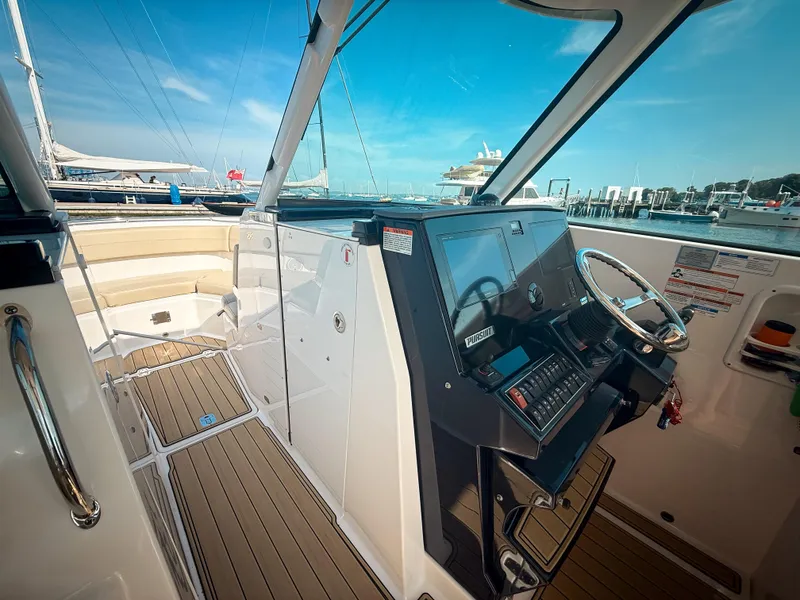 Slide: The Image of 2018 Pursuit DC 325 Dual Console boat interior with helm, steering wheel, and docked marina view. - 28