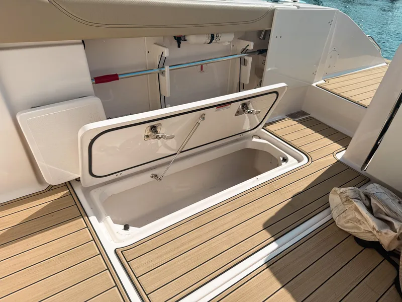 Slide: The Image of 2018 Pursuit DC 325 Dual Console boat storage compartment open on teak deck. - 43