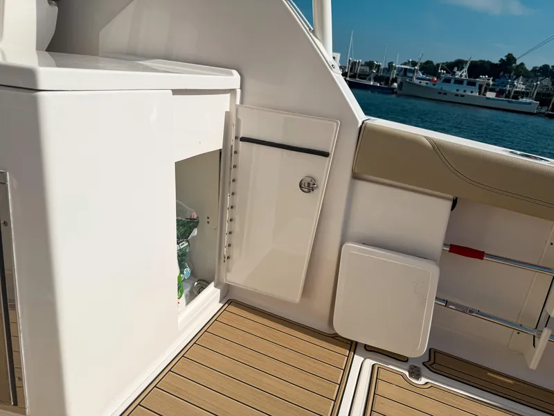 Slide: The Image of 2018 Pursuit DC 325 Dual Console interior with storage compartment, teak flooring, and marina view. - 47