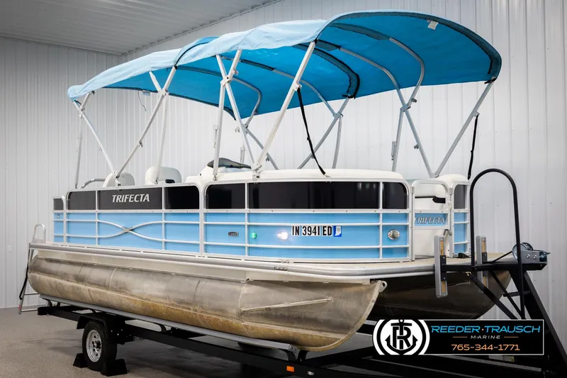 Slide: The Image of 2020 Trifecta 20 RFC CS pontoon boat with blue canopy on trailer in showroom. - 3