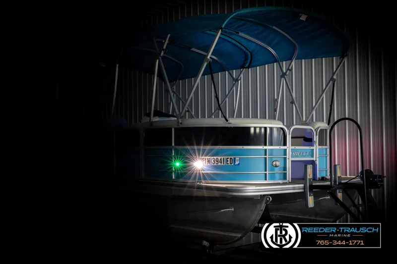 Slide: The Image of 2020 Trifecta 20 RFC CS pontoon boat with blue canopy in dimly lit storage. - 4