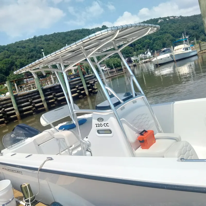 Slide: The Image of 2024 Aquasport 2200 Center Console boat docked by a scenic waterfront. - 12