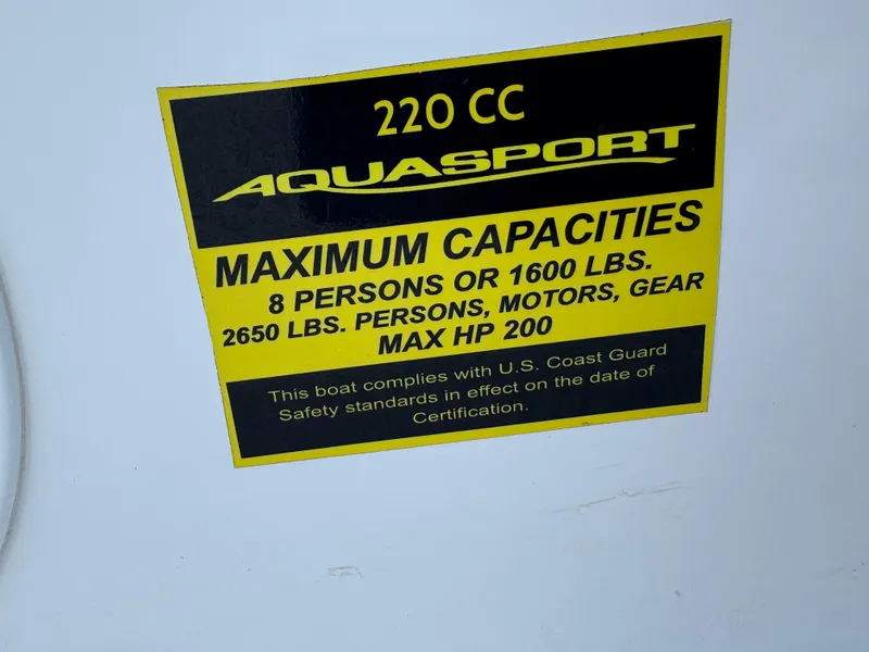 Slide: The Image of Sticker on 2023 Aquasport 2200 Dual Console showing maximum capacities and safety compliance. - 8