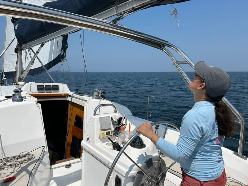 Slide: The Image of Person steering a 2000 Hunter 340 sailboat on open water under clear skies. - 6
