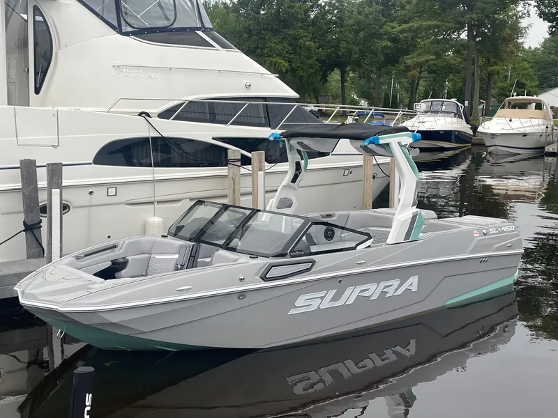 Slide: The Image of 2025 Supra SL boat docked at marina, sleek design, gray color, surrounded by other boats. - 0