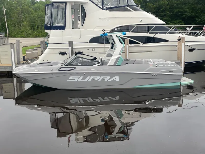 Slide: The Image of 2025 Supra SL boat docked beside larger yacht, reflecting on calm water. - 2