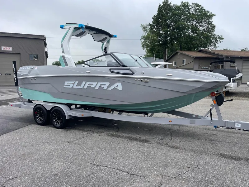 Slide: The Image of 2025 Supra SL boat on trailer, gray and teal design, parked outdoors. - 8