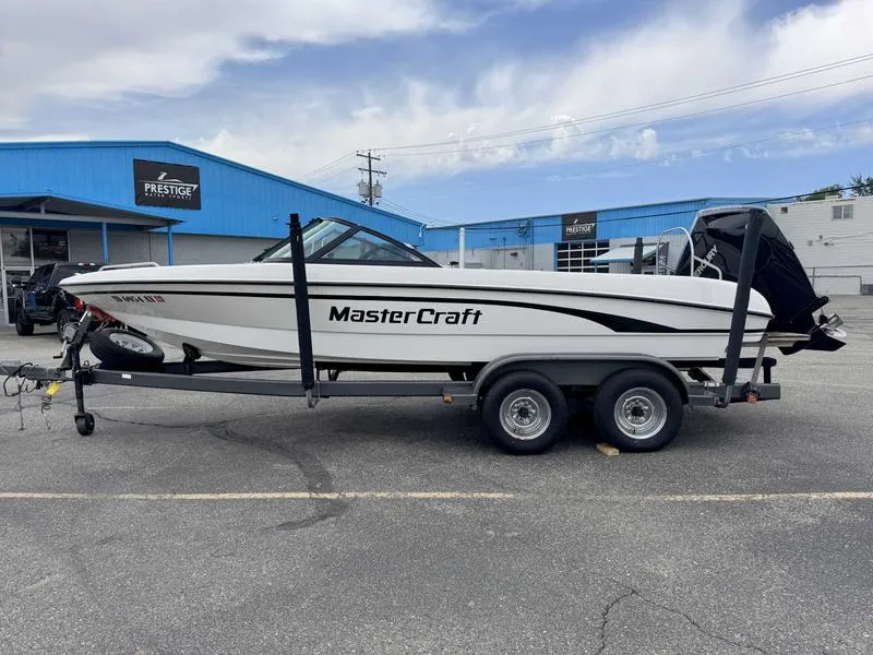 Slide: The Image of 1999 MasterCraft Powerstar 200 boat on trailer in parking lot, blue building background. - 0