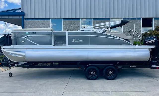 Slide: The Image of 2023 Barletta Cabrio 22UC pontoon boat on trailer, parked outside a building. - 0