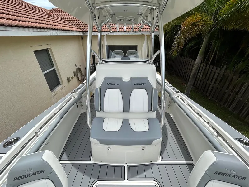 Slide: The Image of 2019 Regulator 23 boat interior with gray and white seating, located near a house and palm trees. - 18