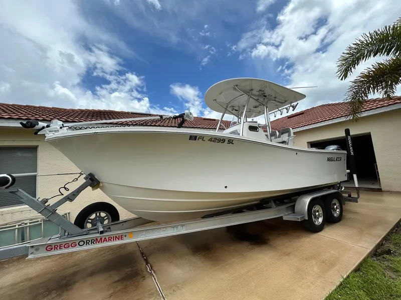 Slide: The Image of 2019 Regulator 23 boat on trailer, parked in driveway under cloudy sky. - 31