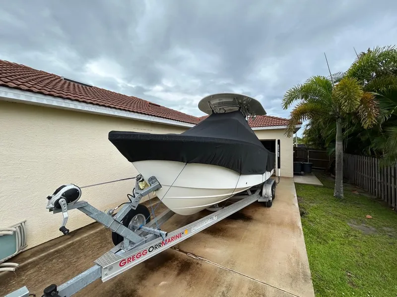Slide: The Image of 2019 Regulator 23 boat on trailer, covered, parked beside a house with palm trees. - 4