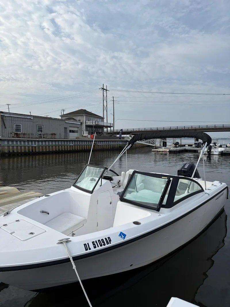 Slide: The Image of 2024 Aquasport 2200 Dual Console boat docked in a marina under cloudy skies. - 4