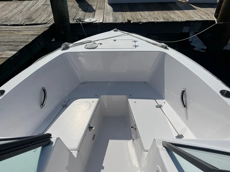 Slide: The Image of 2024 Aquasport 2200 Dual Console boat interior with seating and storage, docked at a wooden pier. - 2