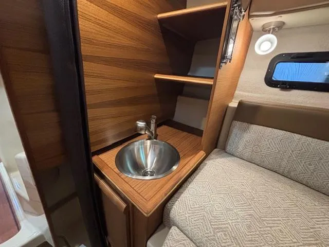 Slide: The Image of 2025 Ranger Tugs R-23 interior with sink, wooden shelves, and cozy seating. - 6