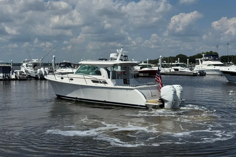 Slide: The Image of 2022 Back Cove 34O boat in marina, surrounded by other vessels, under a partly cloudy sky. - 2
