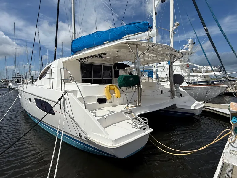Slide: The Image of 2013 Leopard 44 catamaran docked at marina, featuring blue canopy and spacious deck. - 4
