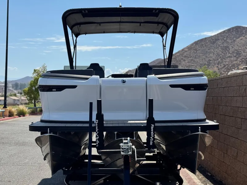 Slide: The Image of 2024 Manitou Explore 24 Navigator pontoon boat, rear view, parked on trailer, scenic mountain backdrop. - 2