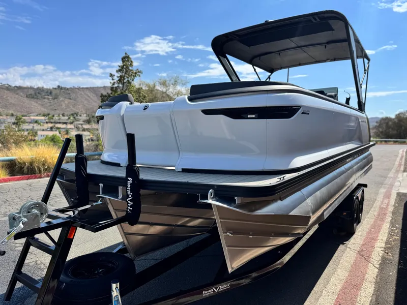 Slide: The Image of 2024 Manitou Explore 24 Navigator pontoon boat on trailer, scenic outdoor setting. - 3