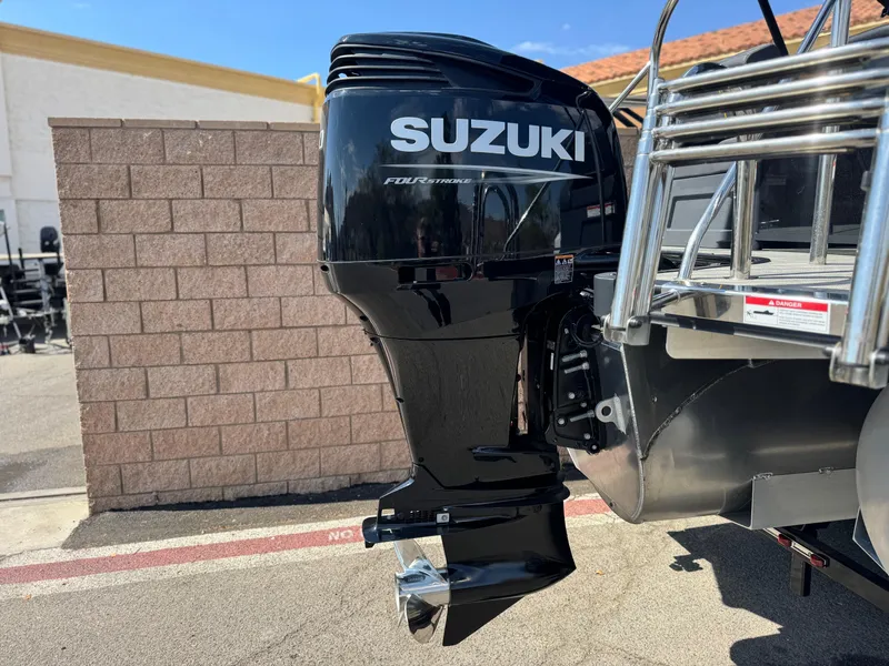 Slide: The Image of 2024 Manitou Explore 24 Navigator with Suzuki outboard motor, parked outdoors. - 7