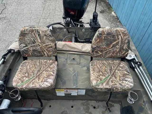 Slide: The Image of 2018 Tracker Grizzly 1648 SC boat with camo seats and motor, parked by a blue wall. - 14