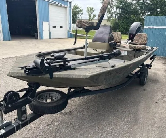 Slide: The Image of 2018 Tracker Grizzly 1648 SC boat on trailer, parked outside a blue building. - 2