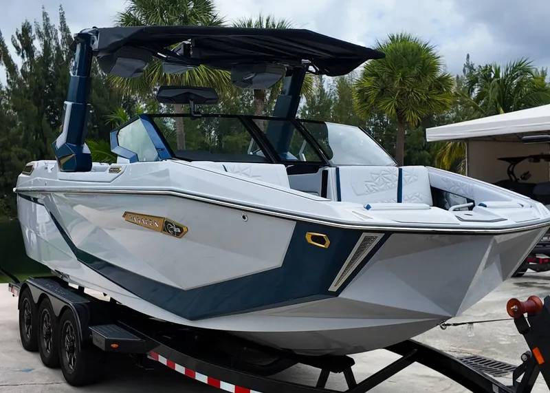 The Image of 2025 Nautique G23 Paragon boat on trailer, surrounded by palm trees. - 0