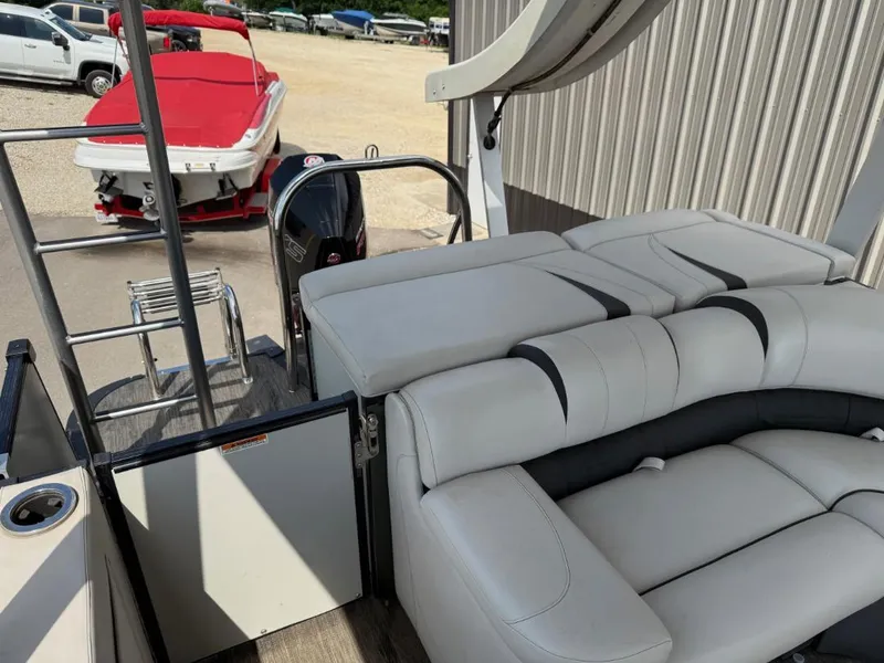 Slide: The Image of 2022 Avalon 2585 CR boat interior with white seating and ladder, parked near a red-covered boat. - 8