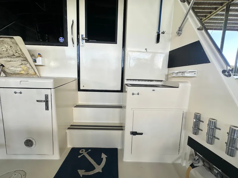 Slide: The Image of 1988 Hatteras Enclosed Bridge Sportfish interior with steps, storage, and nautical-themed mat. - 32