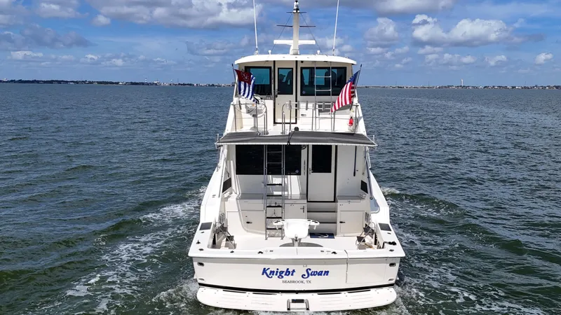 Slide: The Image of 1988 Hatteras Enclosed Bridge Sportfish yacht on open water, rear view with flags. - 15