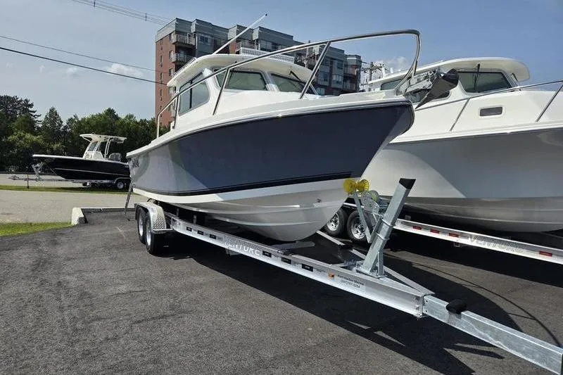 Slide: The Image of 2026 Parker 2220 Sport Cabin boat on trailer, parked outdoors near buildings. - 8