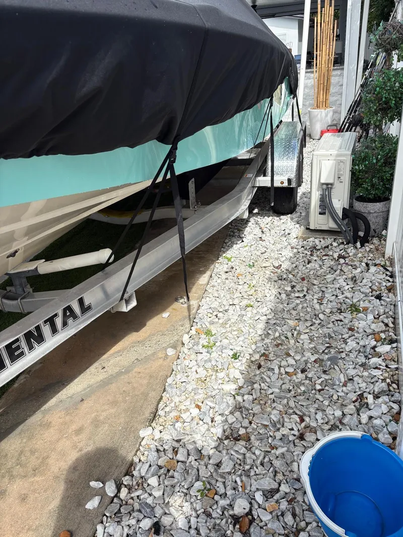 Slide: The Image of Covered BlackJack 224 boat on trailer, parked on gravel, with blue bucket nearby. - 37