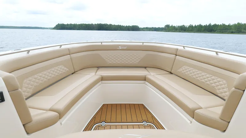 Slide: The Image of 2022 Scout 330 LXF boat interior with tan seating and wooden deck, on a calm lake. - 41