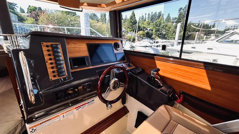 Slide: The Image of 2024 Ranger Tugs R27-OB helm with wood accents, modern controls, and marina view. - 15