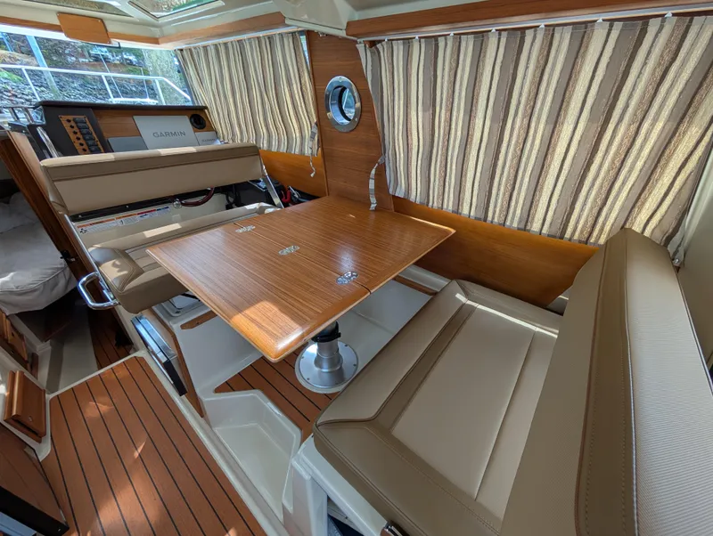 Slide: The Image of 2024 Ranger Tugs R27-OB interior with wood table, striped curtains, and beige seating. - 20