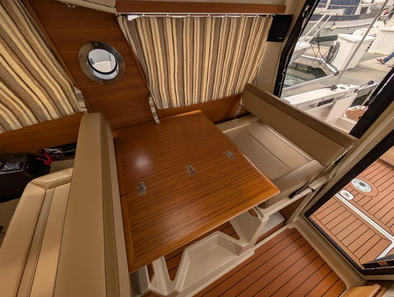 Slide: The Image of 2024 Ranger Tugs R27-OB interior with wood table, beige seating, and striped curtains. - 21
