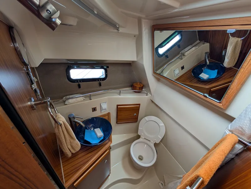 Slide: The Image of 2024 Ranger Tugs R27-OB bathroom with wooden accents, mirror, and blue sink. - 24