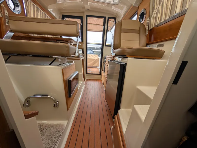Slide: The Image of 2024 Ranger Tugs R27-OB interior with wood flooring, seating, and compact kitchen area. - 25