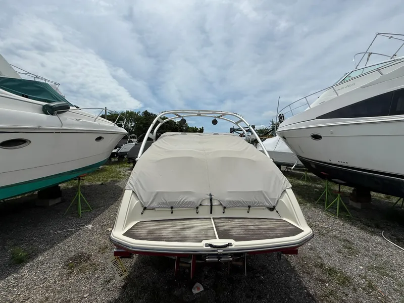 Slide: The Image of 2014 Yamaha Boats 242 Limited S covered, parked between other boats under a cloudy sky. - 7
