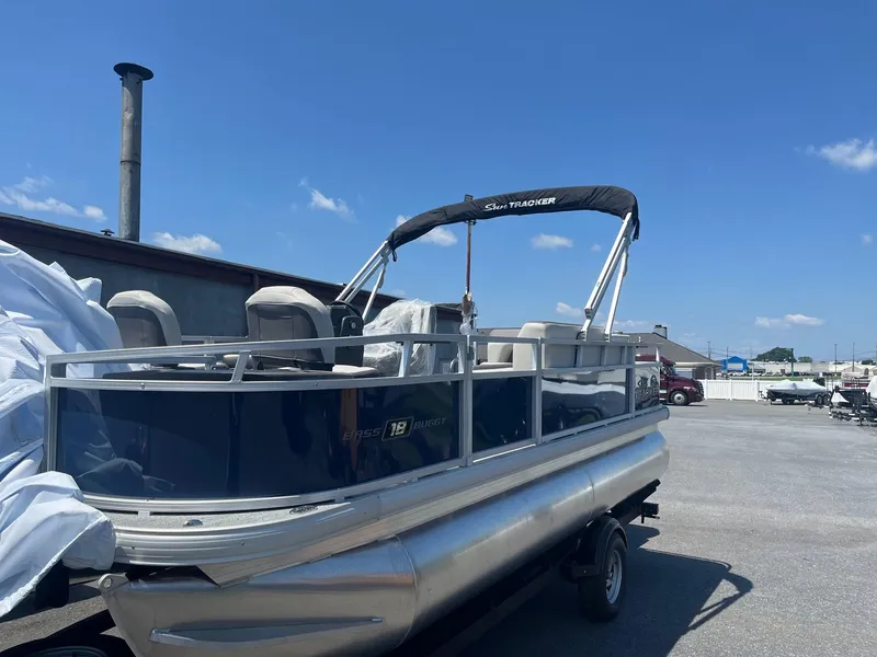 Slide: The Image of 2026 Sun Tracker Bass Buggy 18 DLX pontoon boat parked outdoors under clear blue sky. - 2