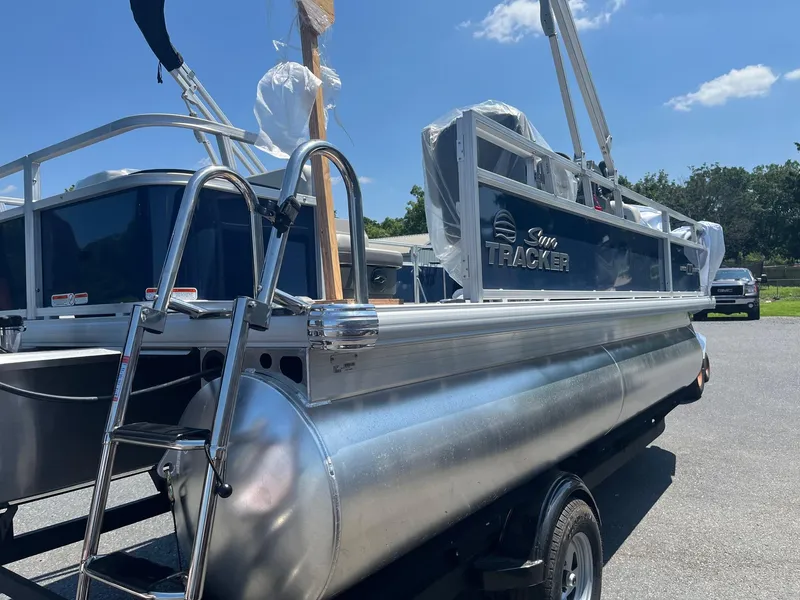 Slide: The Image of 2026 Sun Tracker Bass Buggy 18 DLX pontoon boat with ladder, parked outdoors. - 20